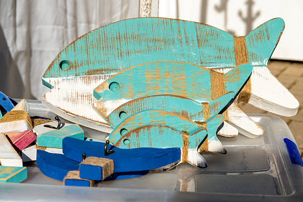 A collection of rustic wooden fish decorations painted in blue and white, featuring distressed textures and twine accents, displayed on a plastic surface.