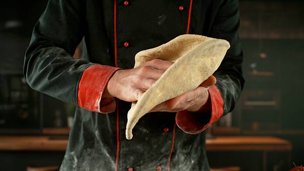 Freeze motion of baker processing yeast dough on pizza.