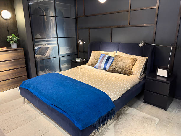 Bedroom interior with stylish soft linen in gray-blue tones, a laptop and a cup of coffee on the bedside table.