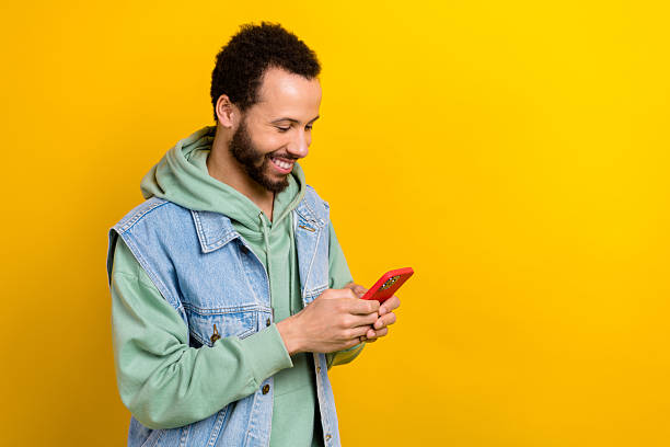 istock Profile photo of nice cheerful guy use smart phone chatting empty space instagram twitter facebook isolated on yellow color background 2214728106