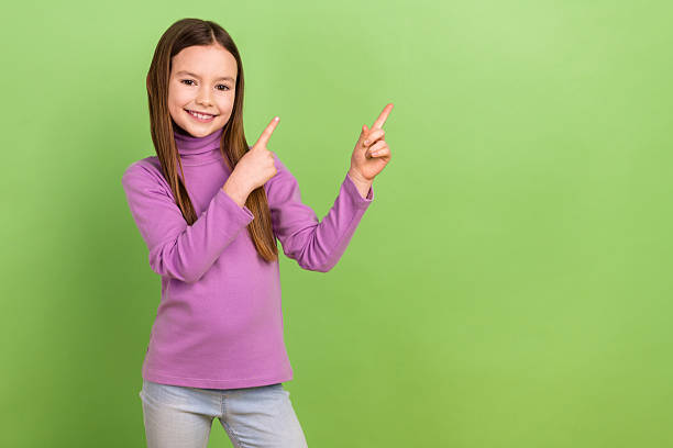 istock Portrait of cheerful diligent schoolgirl dressed violet sweatshirt indicating at empty space discount isolated on green color background 2214730657