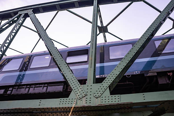 A train traveling over a green steel bridge with structural trusses, viewed from below, emphasizing transportation, infrastructure, and engineering.