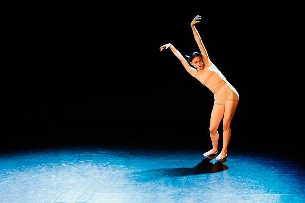 Young woman dancing contemporary dance on a dark stage