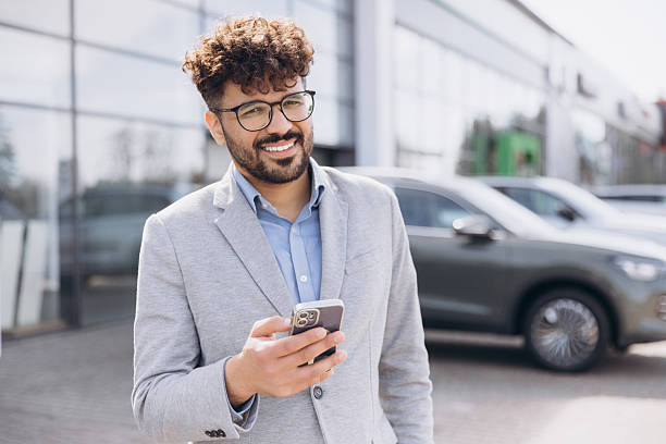 istock Smiling businessman using smartphone outside car dealership 2214738499