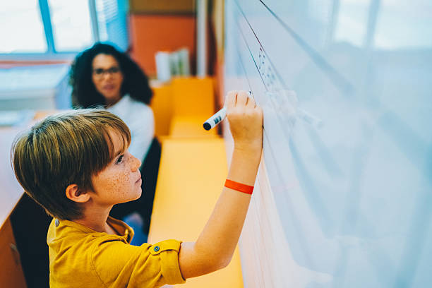 istock Schoolboy writing on whiteboard in classroom 2214739085