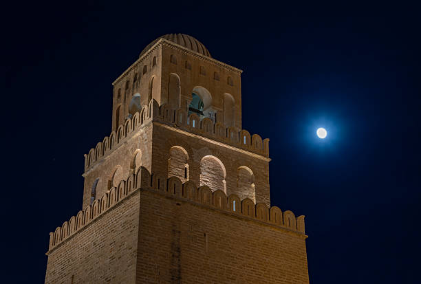 A picture of the Great Mosque of Kairouan at night, with the moon in the distance.