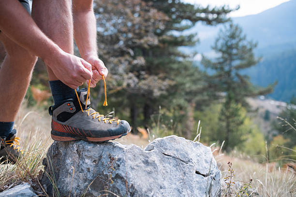 A man ties his hiking boots before starting a trek in a mountainous terrain.