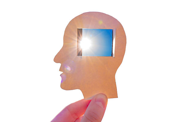 Hand holds a paper cutout of a male head with a square cutout showing bright sunlight, symbolizing mindfulness, creativity, and mental clarity.