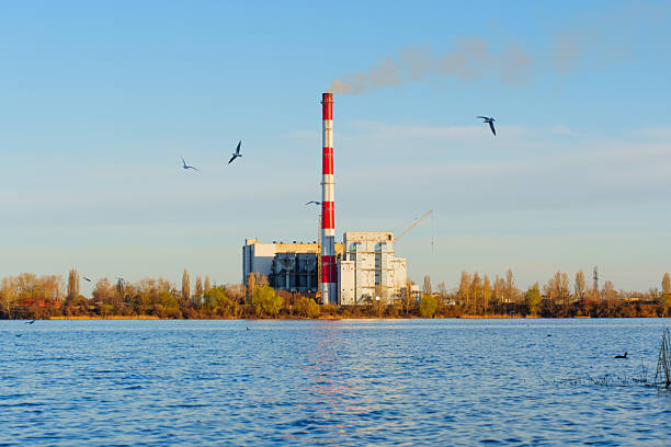 Modern waste incineration plant located by a serene body of water, showcasing smoke emissions and natural surroundings, emphasizing waste management and energy sources.