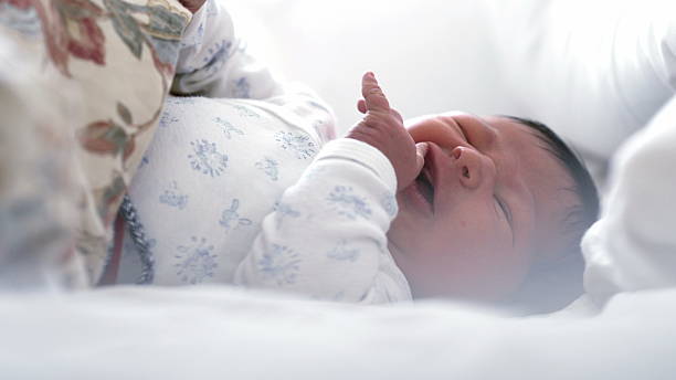 istock Newborn baby lying in bed, gesticulating with hands and making slight grimaces. baby surrounded by soft pillows, creating a cozy and serene atmosphere in the bedroom-SD 480p 2214748012