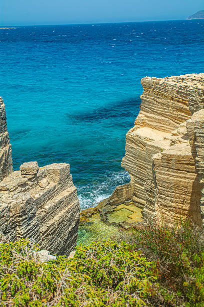 Ancient limestone area on Favignana Island, Sicily, with rugged rock formations, sparse vegetation, and a deep blue sea under a bright sky in the background