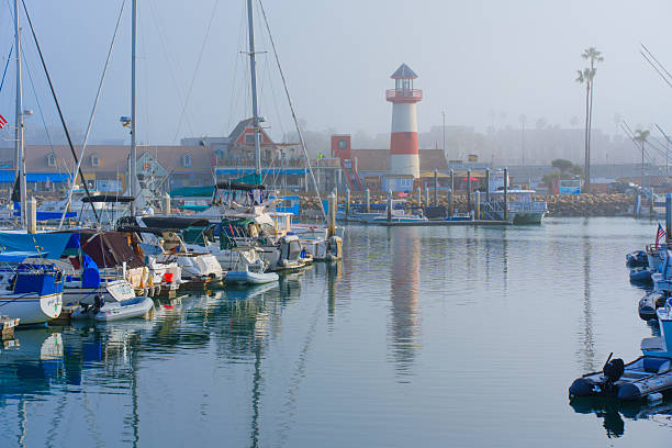 Oceanside, California - January 3, 2025: Tranquil scene of a decorative lighthouse surrounded by boats at Oceanside Harbor, California, captured in soft morning fog with calm waters.