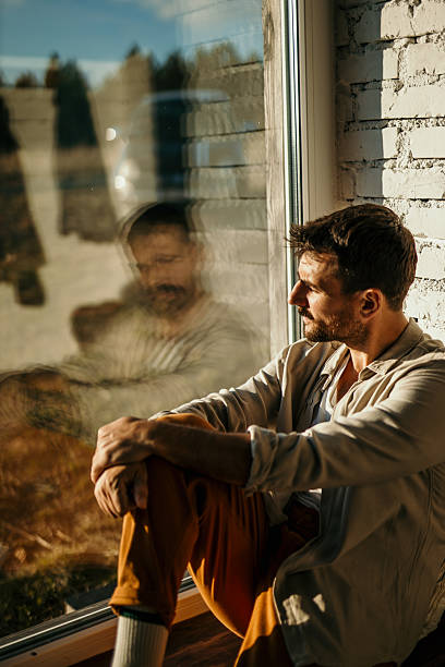 istock Pensive man sitting by window contemplating life 2214752237
