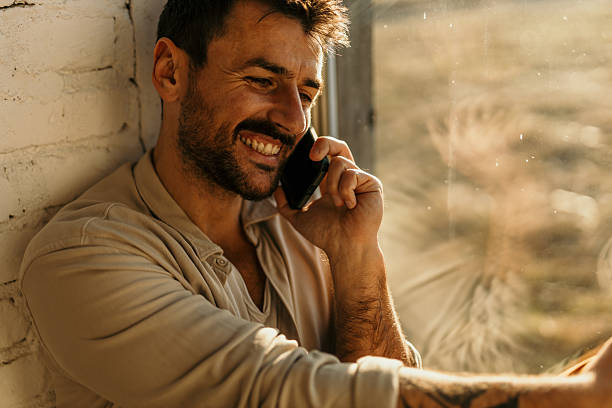 istock Happy man smiling while talking on phone near window 2214752284