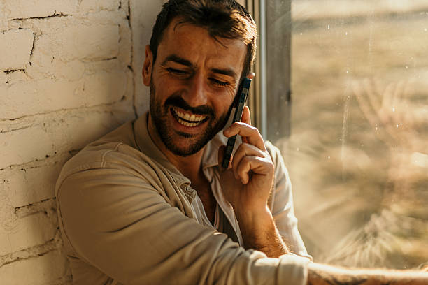 istock Happy man laughing while talking on mobile phone near window 2214752300