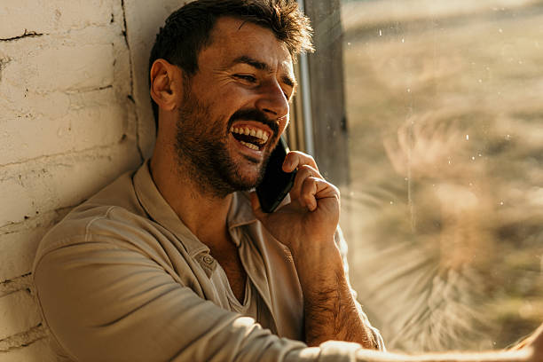 istock Happy man laughing while talking on the phone near a window 2214752308