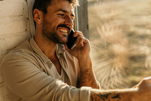 istock Smiling man talking on smartphone by window in natural light 2214752311