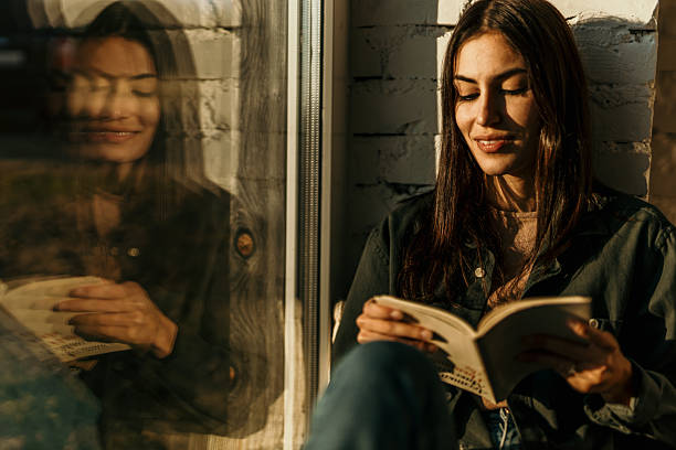 istock Young woman reading a book by the window in sunlight 2214752358