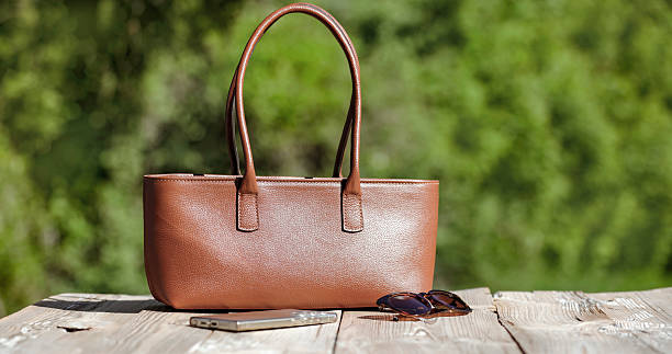 Brown woman handbag on rustic wooden table in natural garden setting. Spring composition in day light.