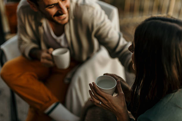 Young couple drinking coffee in cafe and chatting, focus on woman holding cup in her hands
