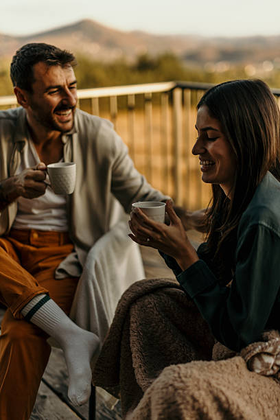 istock Couple laughing and drinking coffee on a balcony overlooking a scenic mountain view 2214752493