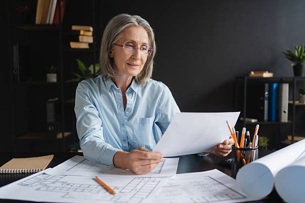 istock Architecture, drawing and blueprint with mature Caucasian woman architect, construction plan for building renovation. Designer, engineering and construction worker with paperwork and planning 2214753638
