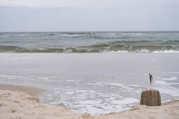 istock Sandcastle with Feather and Red plastic straw near Ocean Waves 2214754922