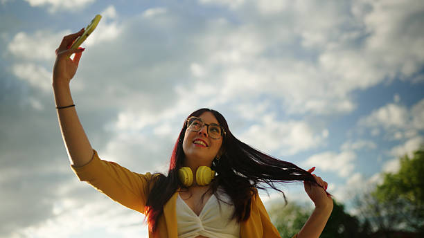 istock Young woman taking a selfie outdoors with cloudy sky while playing with her hair 2214757108