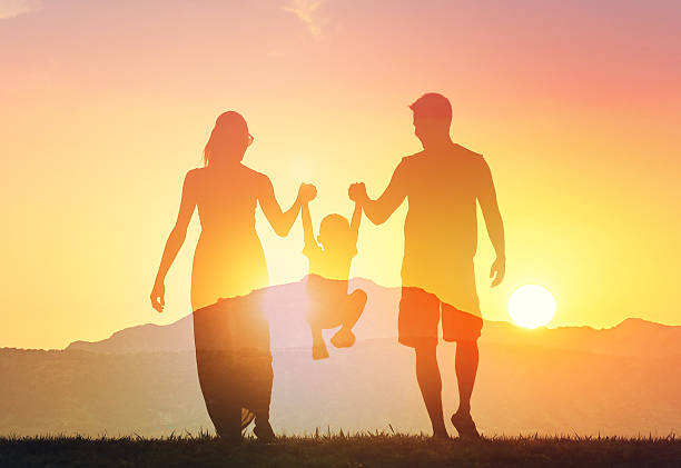 Parents showing child love and support concept. Happy family silhouettes bonding playing in the sunset.