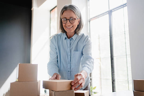 istock Older mature female online store small business owner worker packing package post drop shipping ecommerce retail order in box preparing delivery parcel on table in warehouse. Dropshipping service. 2214760187