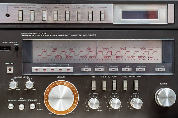 Close-up of a vintage stereo cassette recorder, showcasing its various buttons, knobs, and the electronic clock displaying the radio frequency