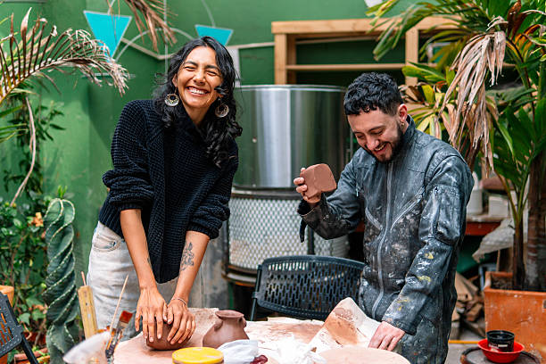 Two joyful potters shaping clay, laughing and enjoying their time together in a vibrant pottery workshop filled with creativity