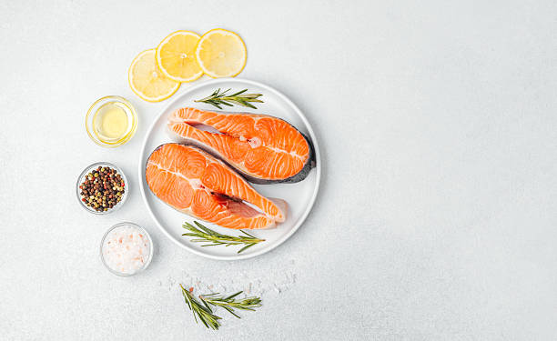 istock Fresh salmon steaks prepared with lemon slices and herbs on a clean surface 2214771968