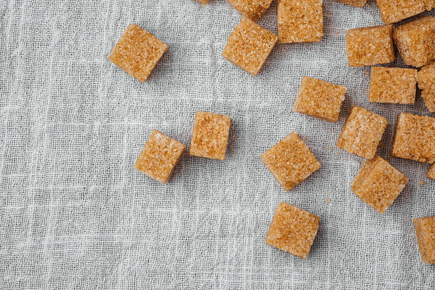 Brown sugar cubes are casually placed on a textured linen cloth, ideal for baking.