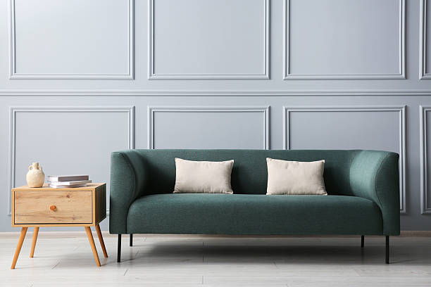 istock Stylish sofa with cushions and books on side table near grey wall 2214772460