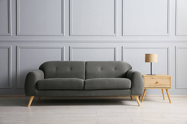 istock Stylish sofa and lamp on side table near grey wall 2214772468