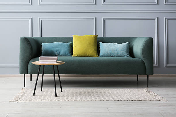istock Stylish sofa with cushions and books on side table near grey wall 2214772471