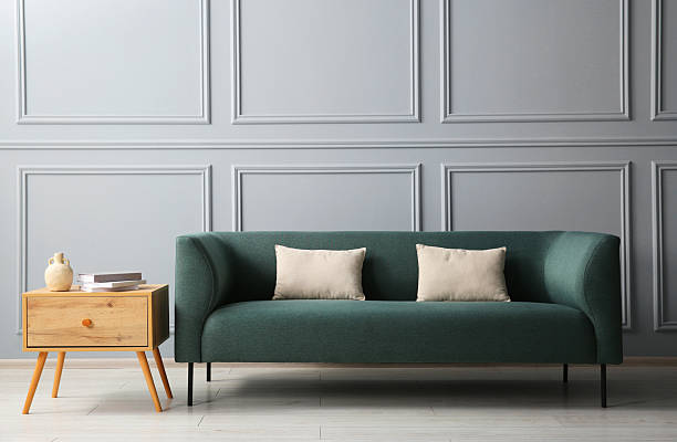 istock Stylish sofa with cushions and books on side table near grey wall 2214772481
