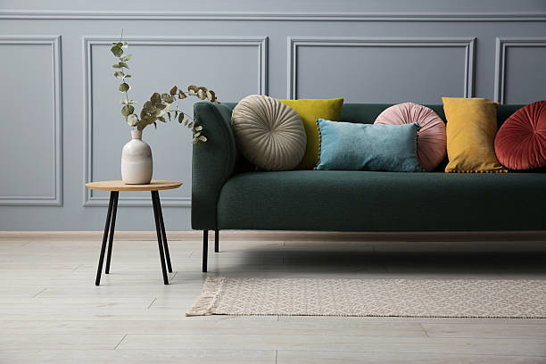istock Stylish sofa with cushions and eucalyptus branches in vase on side table near grey wall 2214772491