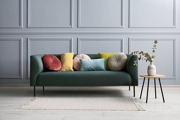 istock Stylish sofa with cushions and eucalyptus branches in vase on side table near grey wall 2214772538