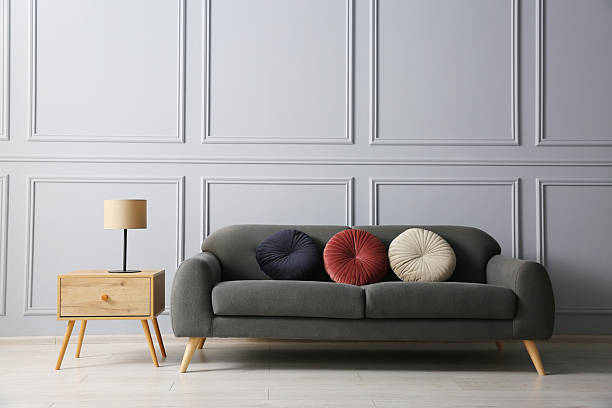 istock Stylish sofa with cushions and lamp on side table near grey wall 2214772546