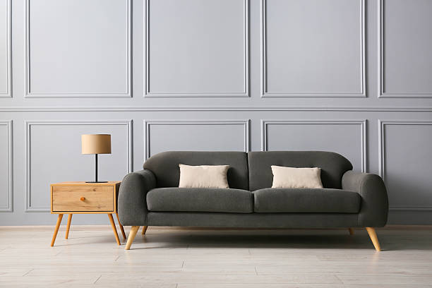istock Stylish sofa with cushions and lamp on side table near grey wall 2214772551