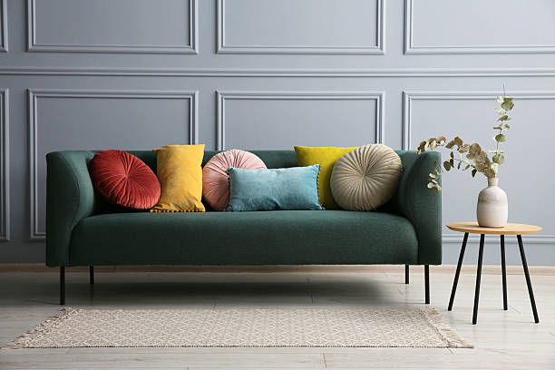 istock Stylish sofa with cushions and eucalyptus branches in vase on side table near grey wall 2214772672