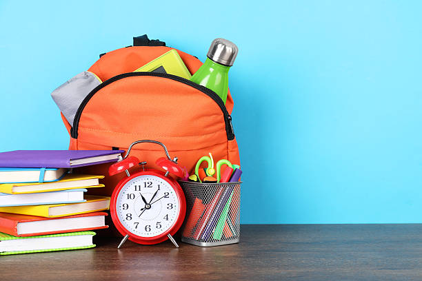 istock Backpack with different school stationery and alarm clock on wooden table against light blue background. Space for text 2214773775