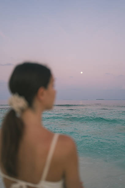 Rear view of young woman looking out to sea on tropical beach at sunset, selective focus on background