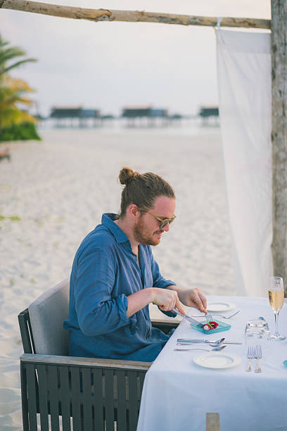 istock Young man enjoys meal at beach restaurant at sunset 2214776771