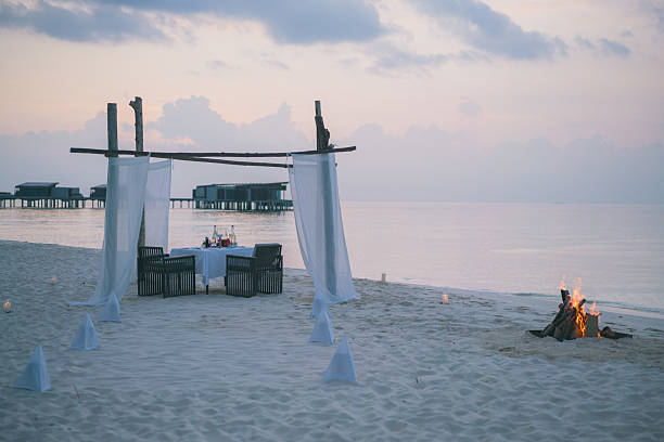 Restaurant on edge of sea at sunset, beach fire beside, luxury resort, medium distance