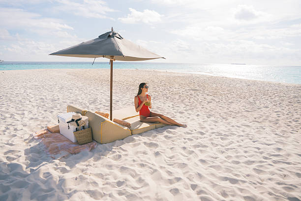 Young woman sips a fresh coconut on a lounge chair, under a beach umbrella at luxury resort