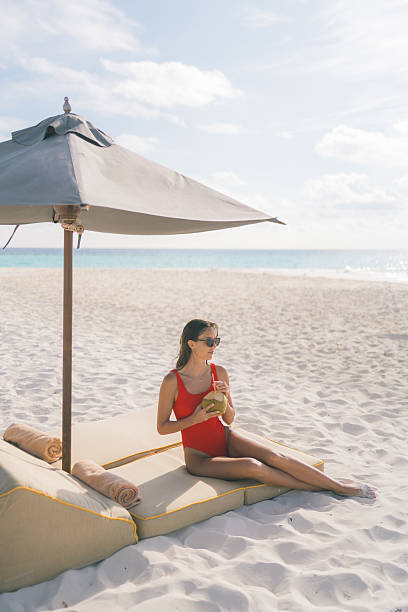 Young woman sips a fresh coconut under a beach umbrella