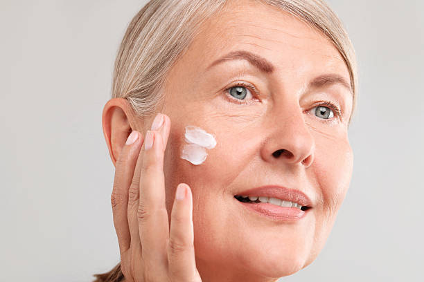 istock Senior woman applying face cream on light background, closeup 2214778917